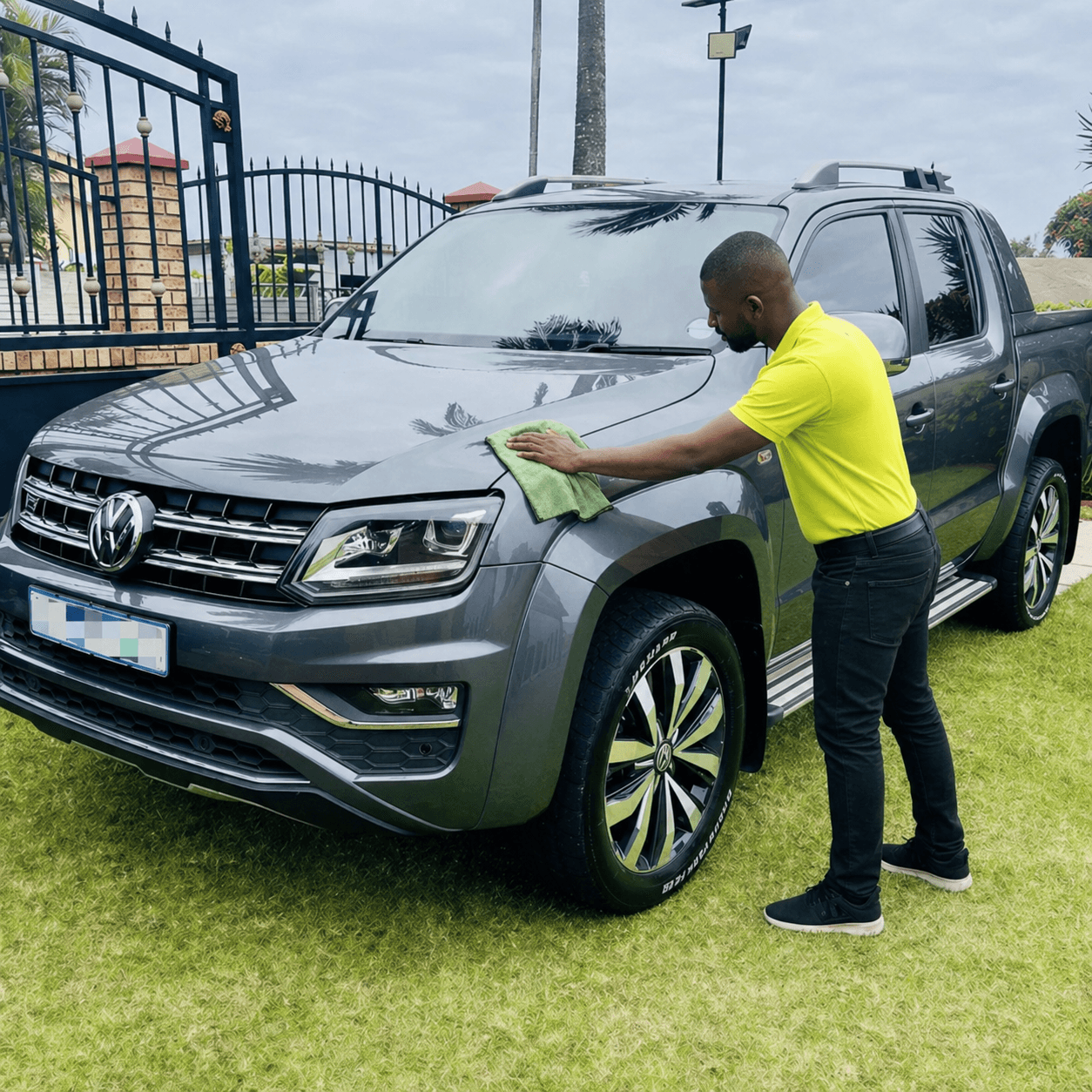 Man in yellow shirt cleaning the hood of a grey Volkswagen pickup truck.