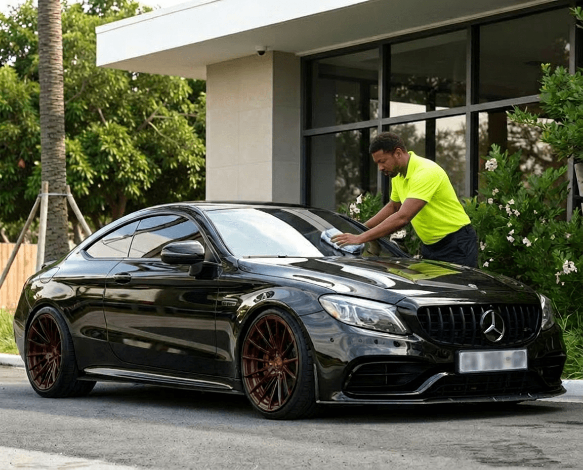 Man in neon yellow shirt cleaning a black Mercedes-Benz coupe with custom bronze rims.