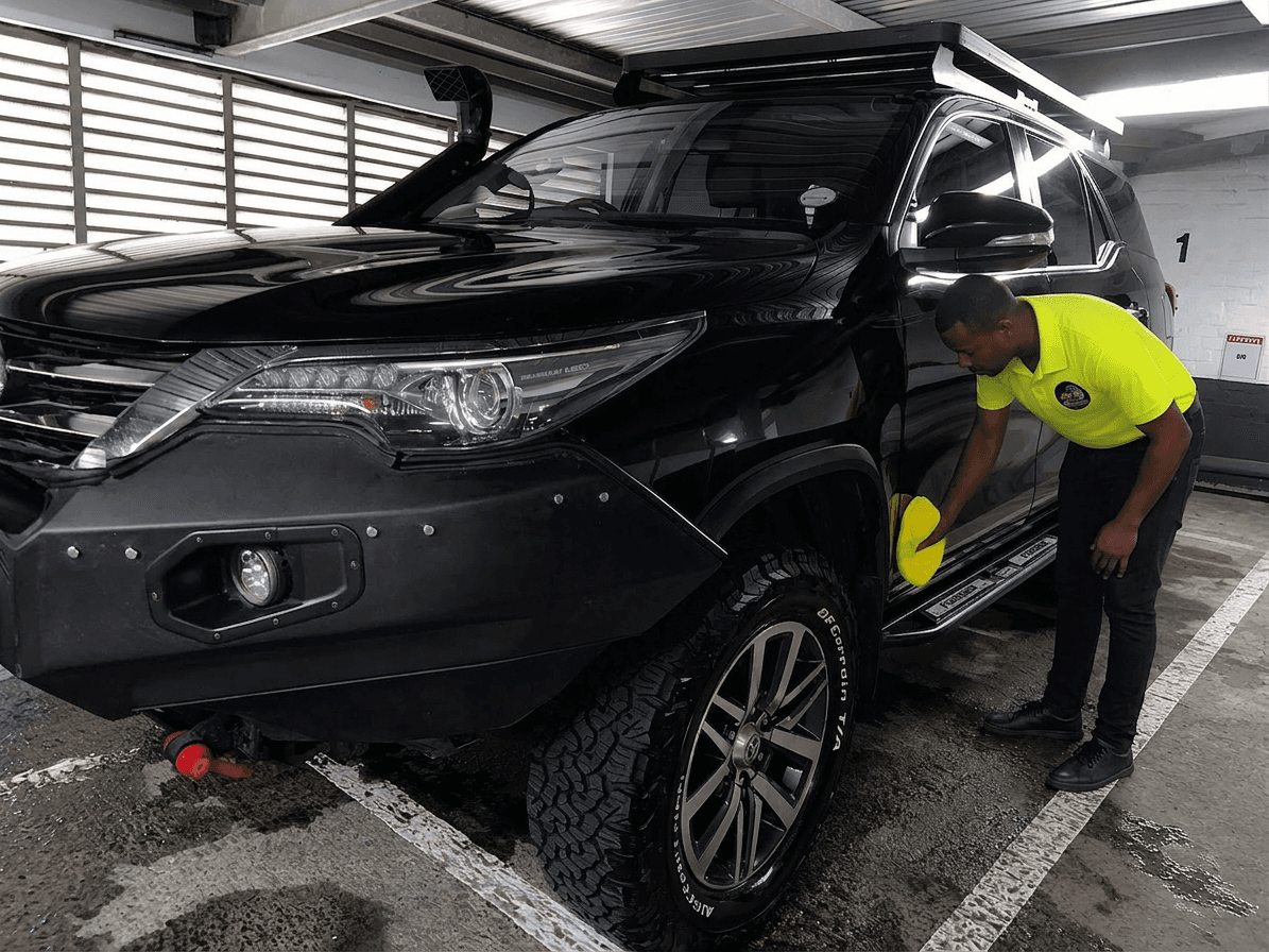 Man in neon yellow shirt detailing a black off-road SUV with a yellow cloth.